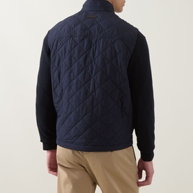 Model wearing Gant Classic Diamond Quilted Gilet in Evening Blue, rear view, styled with navy knit sleeves and beige trousers.