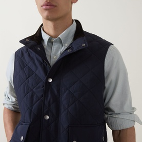Model wearing Gant Classic Diamond Quilted Gilet in evening blue, with snap buttons and high neckline, styled over a grey chambray shirt.