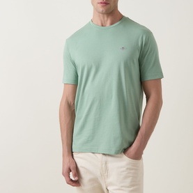 Model wearing Gant Shield Logo T-Shirt in Surplus Mint, crew neck, short sleeves, small shield logo on chest, styled with cream trousers.