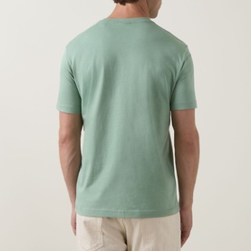 Model wearing Gant Shield Logo T-Shirt in Surplus Mint, rear view, crew neck, short sleeves, paired with beige trousers.