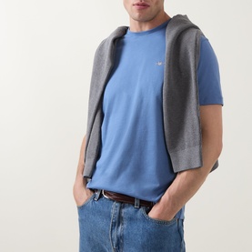 Model wearing Gant Shield Logo T-Shirt in Blue Horizon, crew neck, short sleeves, styled with grey gilet and jeans.