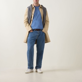 Model wearing Gant Shield Logo T-Shirt in Blue Horizon, styled with beige trench coat, blue jeans, and white trainers.