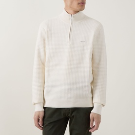 Model wearing Gant Logo Textured Half-Zip Sweater in cream with waffle-knit texture, half-zip neck and embroidered logo, styled with khaki trousers.