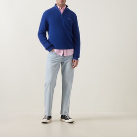 Model wearing Gant Shield Logo Half-Zip Micro Textured Sweatshirt in Crisp Blue, styled with pink shirt, light grey trousers and black trainers.