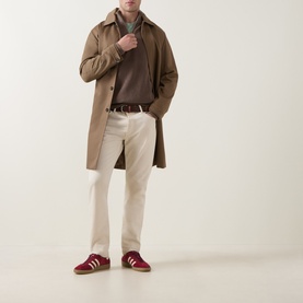 Model wearing Gant Shield Logo Half-Zip Sweatshirt in Dark Hazelnut Melange, styled with a camel overcoat, cream trousers and burgundy trainers.