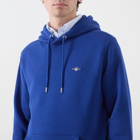 Model wearing Gant Shield Drawstring Hoodie in Crisp Blue, with embroidered shield logo, drawstring hood, styled over collared shirt.