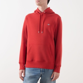 Model wearing Gant Shield Drawstring Hoodie in Maple Fire, styled with light blue denim jeans. Kangaroo pocket and shield logo visible.