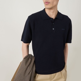 Model wearing Gant Evening Blue cotton textured knit polo shirt, styled with beige trousers and a houndstooth jacket draped over arm.