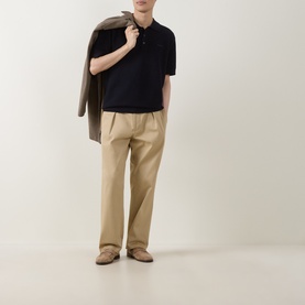 Model wearing Gant Evening Blue cotton knit polo, styled with beige wide-leg trousers and a grey jacket draped over shoulder.