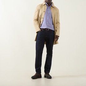 Model wearing Gant Crisp Blue Reg Shirt in cotton, styled with beige mac coat, dark navy jeans and brown leather shoes