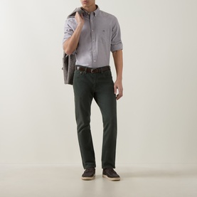 Model wearing Gant Shield Logo Oxford Shirt in Faded Taupe with dark green trousers and brown belt, carrying a jacket over one shoulder.