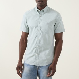 Model wearing Gant Shield Logo Shirt in Surplus Mint, short sleeves, button-down collar, chest pocket, paired with light-wash jeans.