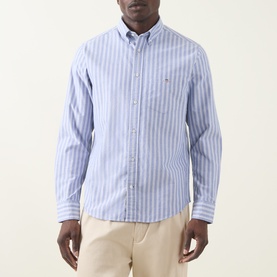 Model wearing Gant Shield Logo Striped Shirt in College Blue, button-down collar, long sleeves, styled with beige chinos.