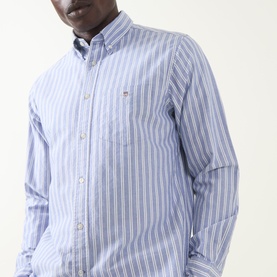 Model wearing Gant Shield Logo Striped Shirt in College Blue, featuring button-down collar, chest pocket, and long sleeves.