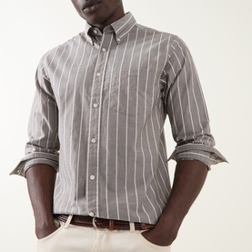 Model wearing Gant Logo Striped Shirt in brown melange, long sleeves rolled at cuffs, button-down collar, chest pocket, paired with cream trousers