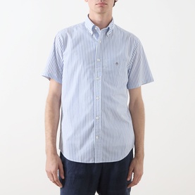 Model wearing Gant Reg Shirt in fresh blue vertical stripe, short sleeves, button-down collar with chest pocket, styled with navy trousers.