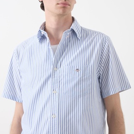 Model wearing Gant Reg Shirt in fresh blue vertical stripe, short sleeves, chest pocket with logo, white base fabric.