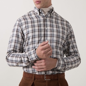 Model wearing Gant Reg Shirt in sand plaid check, styled with a cream roll-neck and brown corduroy trousers, adjusting cuff.