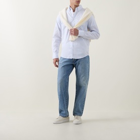 Model wearing Gant light blue cotton Reg Shirt, styled with mid-wash jeans, cream scarf draped over shoulder, and white trainers.