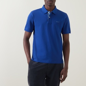 Model wearing Gant Contrast Collar Logo Polo Shirt in Crisp Blue with contrast collar detail, paired with dark navy trousers.