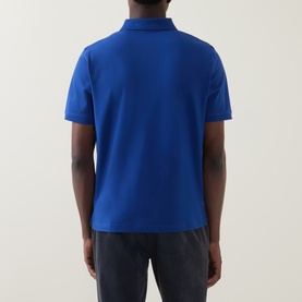 Model wearing Gant Contrast Collar Logo Polo Shirt in Crisp Blue, rear view, short sleeves, straight hemline, styled with dark trousers.