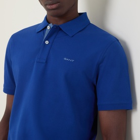 Model wearing Gant Contrast Collar Logo Polo Shirt in Crisp Blue, featuring contrast collar detail and button fastenings, short sleeves visible.