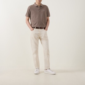 Model wearing Gant Regular Polo in Dark Hazelnut Melange, styled with cream trousers, brown belt, and white trainers.