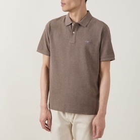 Model wearing Gant Regular Polo in Dark Hazelnut Melange, short sleeves, chest logo, styled with cream trousers.