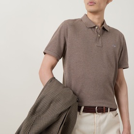 Model wearing Gant Regular Polo in Dark Hazelnut Melange, styled with cream trousers, brown belt, and check blazer draped over arm.
