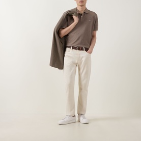 Model wearing Gant Regular Polo in Dark Hazelnut Melange, styled with cream trousers, brown belt, and white trainers, jacket over shoulder.