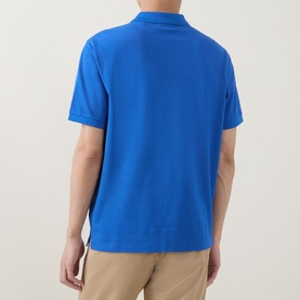 Model wearing Gant Regular Polo in Nautical Blue, short sleeves, rear view, styled with beige trousers.