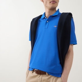 Model wearing Gant Regular Polo in Nautical Blue cotton piqu&eacute;, styled with a navy gilet draped over shoulders and beige chinos.