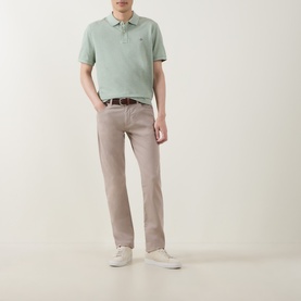 Model wearing Gant Regular Polo in Soft Green Melange, styled with taupe trousers, brown belt and white trainers.