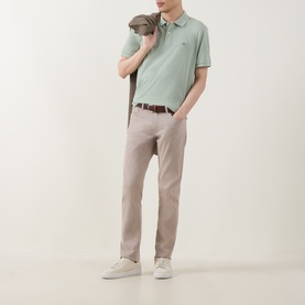 Model wearing Gant Regular Polo in Soft Green Melange, styled with stone chino trousers, brown belt, and white trainers.