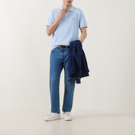 Model wearing Gant Fresh Blue Regular Polo with mid-wash jeans and white trainers, carrying navy jacket over arm.