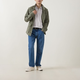 Model wearing Gant Shield Logo Pique Polo Shirt in Glacier Melange, styled with olive field jacket, blue straight jeans and white trainers.