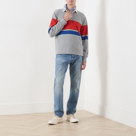 Model wearing Gant Blocked Stripe Rugby Shirt in grey melange with red and blue chest stripes, styled with light wash jeans and white trainers.