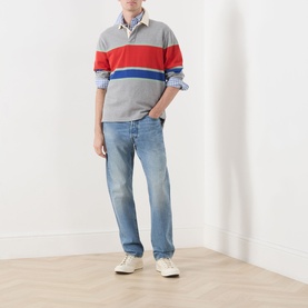 Model wearing Gant Blocked Stripe Rugby Shirt in grey melange with red and blue stripes, styled with light wash jeans and white trainers.