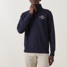 Model wearing Gant Evening Blue half-zip sweatshirt with chest logo embroidery, styled with cream trousers.