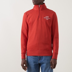 Model wearing Gant Maple Fire quarter-zip sweatshirt with chest logo, styled with blue jeans.