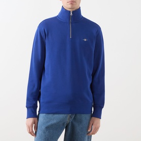 Model wearing Gant Crisp Blue cotton half-zip sweatshirt with funnel neck and embroidered logo, styled with light blue jeans.