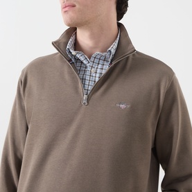 Model wearing Gant faded taupe quarter-zip sweatshirt with embroidered logo, styled over a blue check shirt.