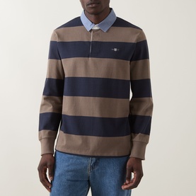 Model wearing Gant Stripe Heavy Rugger Shirt in Faded Taupe, navy block stripes, classic collar, embroidered shield logo, styled with blue jeans.