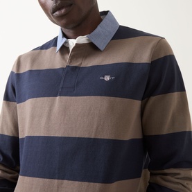 Model wearing Gant Stripe Heavy Rugger Shirt in faded taupe and navy stripe, with embroidered shield logo and classic collar