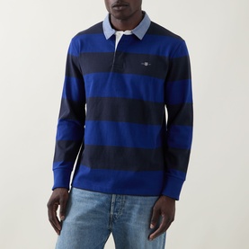 Model wearing Gant Shield Logo Striped Rugby Shirt in Crisp Blue, navy block stripes, contrast collar, long sleeves. Styled with light blue jeans.