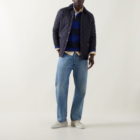 Model wearing Gant Shield Logo Striped Rugby Shirt in Crisp Blue, styled with navy quilted jacket, light-wash jeans and white trainers.