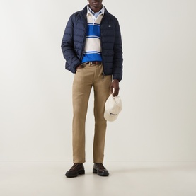 Model wearing Gant Nautical Blue cotton sweatshirt with navy puffer jacket, tan chinos and brown loafers, holding a cap.