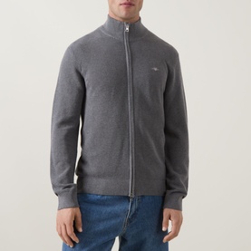 Model wearing Gant Shield Logo Zip Sweater in dark grey melange, full-zip, ribbed trims, small shield logo. Styled with blue jeans.