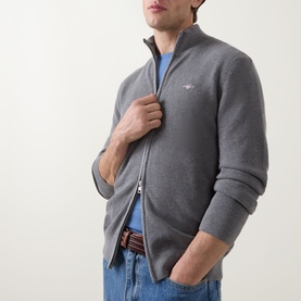 Model wearing Gant Shield Logo Zip Sweater in dark grey melange, zip-through knit with ribbed trims and shield logo, styled with blue jeans.