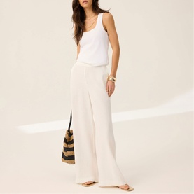 Model wearing Mint Velvet White Scalloped Trim High-Rise Linen Trousers with a white vest top, styled with a striped tote bag.